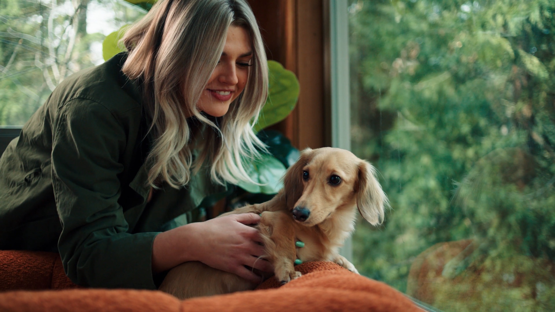 A smiling pet parent embracing her long-haired dachshund at home